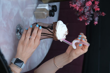 Female hands with a manicure holding a milkshake with chocolate and whipped cream
