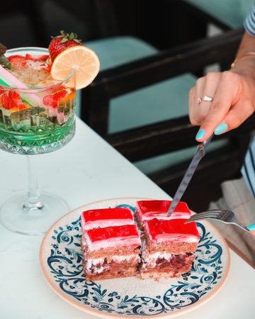 Closeup of a female hand cutting a piece of strawberry cake with a knife
