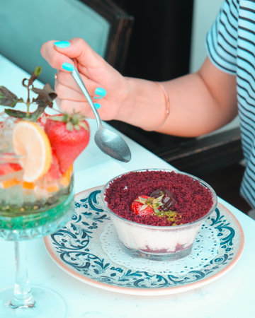 Closeup of a woman's hand with blue manicure holding a spoon and eating a dessertの写真素材
