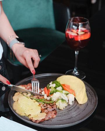 Woman's hands with a knife and fork cut a piece of meat on a plate in a restaurantの写真素材