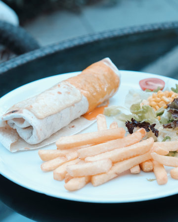 Tortilla wrap with french fries and salad on the table.