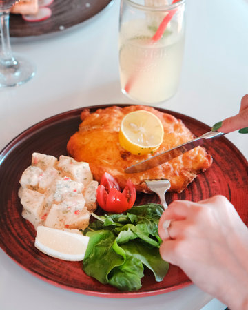 Fish and chips served on a red plate with lemon and salad.の写真素材