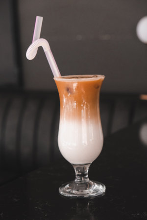 A layered coffee drink with a straw on the tableの写真素材