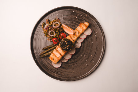 Fried sea bream fish on white plate with onion, garden rocket and lemon slicesの写真素材