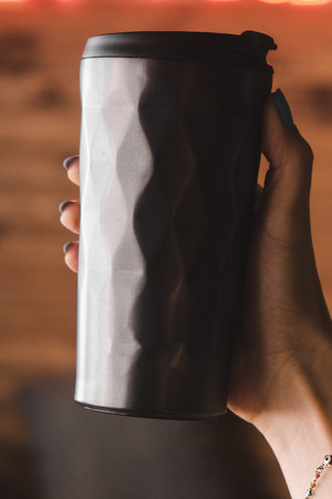 Female hand holding a black metal thermo cup on a wooden background