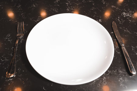 Empty white plate with cutlery on black marble table. top view