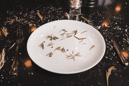 White plate with dried rosemary, sprigs of rosemary on the table