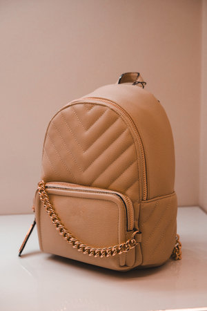Brown leather backpack with gold chain on the white table and brown wall