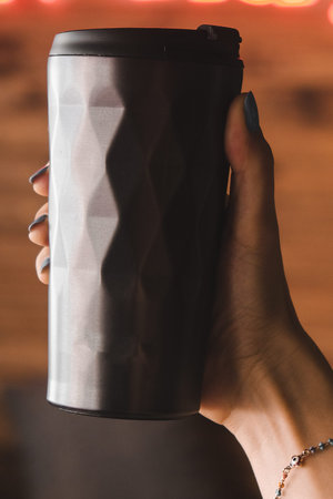 Close up of female hand holding takeaway coffee cup on blurred background.