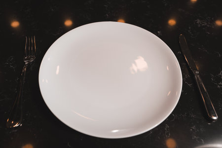 Empty white plate with fork and knife on black table, top viewの写真素材