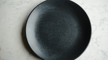 Empty black plate on white marble table, top view, copy space