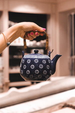 Female hand holding a teapot on the background of the kitchenの写真素材