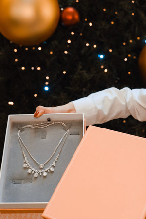 Close-up of a woman's hand holding a gift box with a pearl necklace