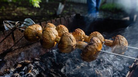 Yummy marinated mushrooms strung on skewers cooked on the grill. Marinated shashlik preparing on a barbecue grill over charcoal, fried to a golden crust.の写真素材