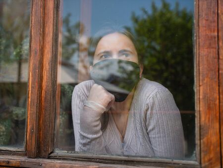 A girl quarantined at home looking outside because of covid19.の写真素材