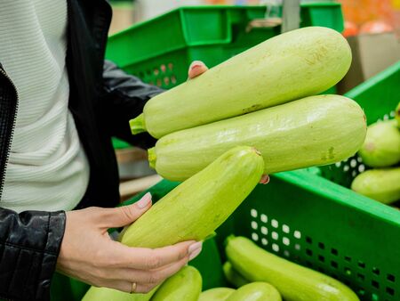 Green, white zucchini in black boxes. Vegetables in the supermarket. A woman chooses zucchiniの写真素材