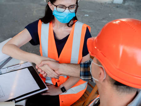 Builders in helmets, vests and medical masks shake hands after signing the contract for the construction of the buildingの写真素材