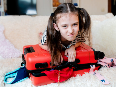 little girl leaned on top of the suitcase trying to close it. A suitcase full of things does not...