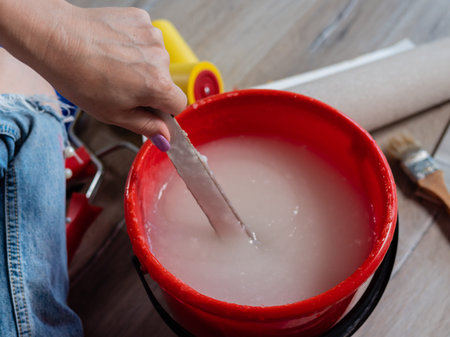 Close-up of a woman kneading glue in a bucket for wallpapering. Renovation of the room and the...