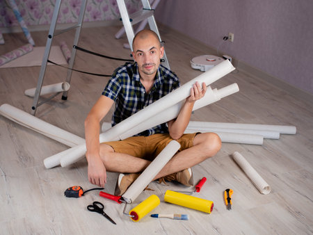 Portrait of a man on the floor with rolls of Wallpaper in his hands on the background of a...