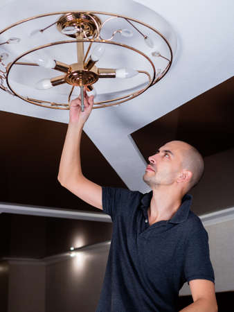 a man spins an LED lamp into a ceiling chandelierの写真素材