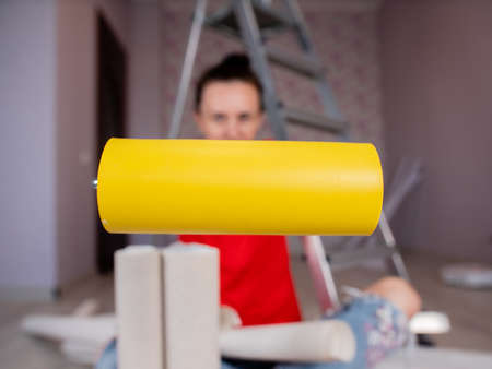 Close-up of a yellow roller for smoothing the wallpaper in the hands of a woman on the background.の写真素材