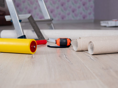 Close-up the measuring tape and the Wallpaper smoothing roller are lying on the floor next to the...