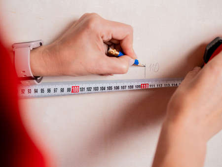 Repairs in the apartment. Close-up of a tape measure and pencil in womens hands. Measuring the walls in a room.の写真素材