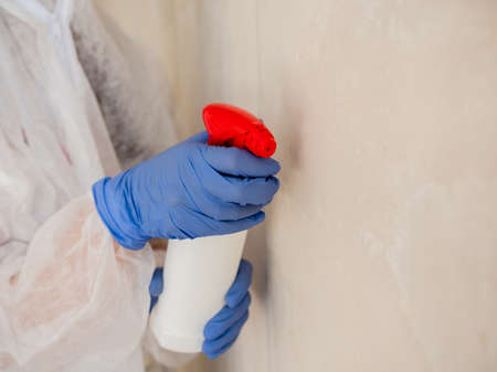 A woman in a protective suit, using a spray gun to spray the affected walls with mold.の写真素材