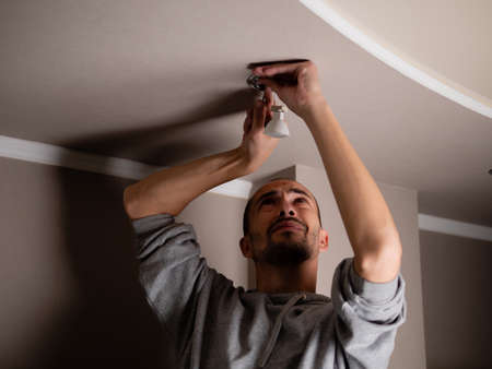 The process of replacing a damaged LED lamp with a downlight. A man in the dark repairs a ceiling soffitの写真素材