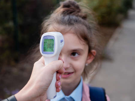 A cheerful Little Girl is being checked outside the schools temperature as it reopens following the COVID-19 pandemic quarantine. Checking body temperature with a non-contact thermometer.の写真素材