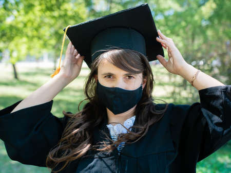 A student in a mantle and a protective medical mask stands in the park of the universityの写真素材