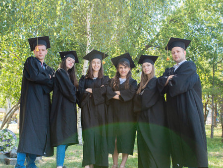 Happy University graduates in robes and academic caps stand in the park
