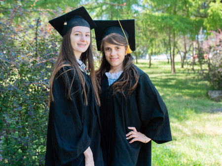 Portrait of two happy graduates in a mantle and an academic cap. Graduated college graduates stand in the parkの写真素材