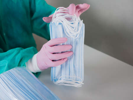 Close-up of a gloved woman counting blue masks at a table.の写真素材