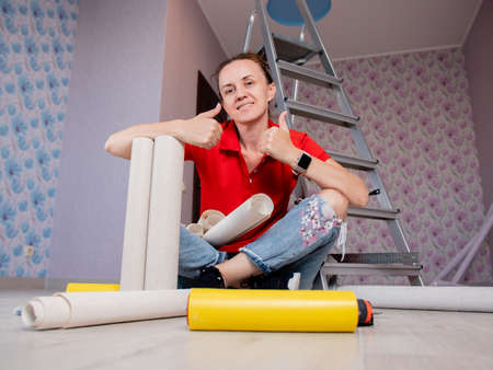 A woman is sitting on the floor in a room with rolls of Wallpaper. Concept of renovation in the apartment.の写真素材