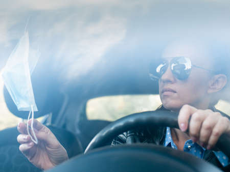 The woman is annoyed in the car. Stuck in traffic. The medical mask hangs on the rearview mirror in the carの写真素材