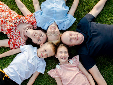 Close-up camera of a mother, father and children who are lying on the lawn, touching each others heads, holding hands and laughing merrily.の写真素材