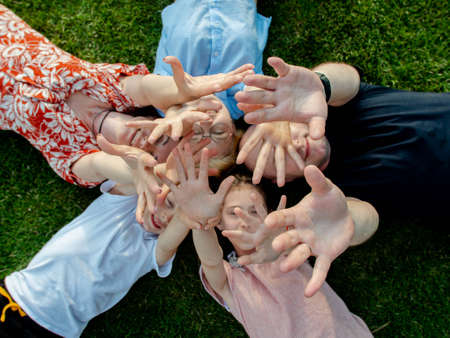 Camera top view of a family with three children and parents lying on the lawn, their heads touch each other, they laugh and point their hands to the sky.の写真素材