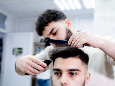 Happy young guy getting a haircut by a professional male hairdresser in a barbershopの写真素材