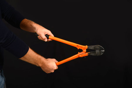Hands with tool bolt cutters on black background