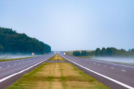 Morning before sunrise. The long highway goes into the distance. Misty fields at the edge of the road.の写真素材