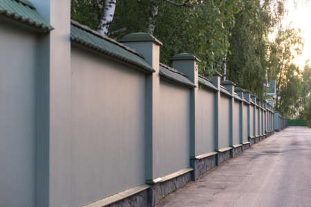 Solid concrete fence. Fence and paved road. Fenced territory, private property.の写真素材