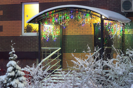 Entrance to the house with a garland. A multicolored garland hangs behind the snow bushes under the roof of the entrance. New Year's entrance to the house.の写真素材