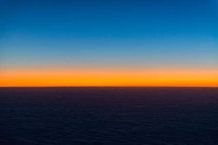 Sunrise from the window of the plane. The horizon is colored by the orange light of the sun. The first rays of the rising sun.の写真素材