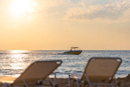 The backs of the sun loungers in front of the sea with a boat. Evening on the beach. Focus on the boat.の写真素材