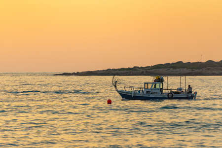 A fishing boat goes out to sea at sunset. A small boat leaves the bay for evening fishing.の写真素材
