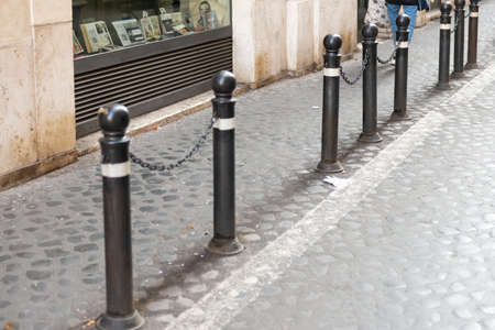 Anti-parking posts with chains. Metal posts separate the sidewalk and the roadway on the cobblestone pavement.の写真素材