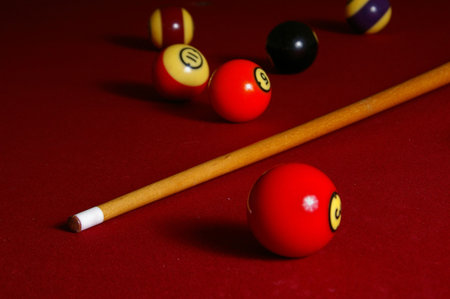 A pool cue and balls rest on a red felt table