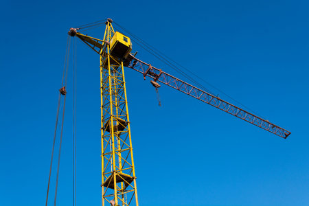 a yellow tower crane in operation against blue sky